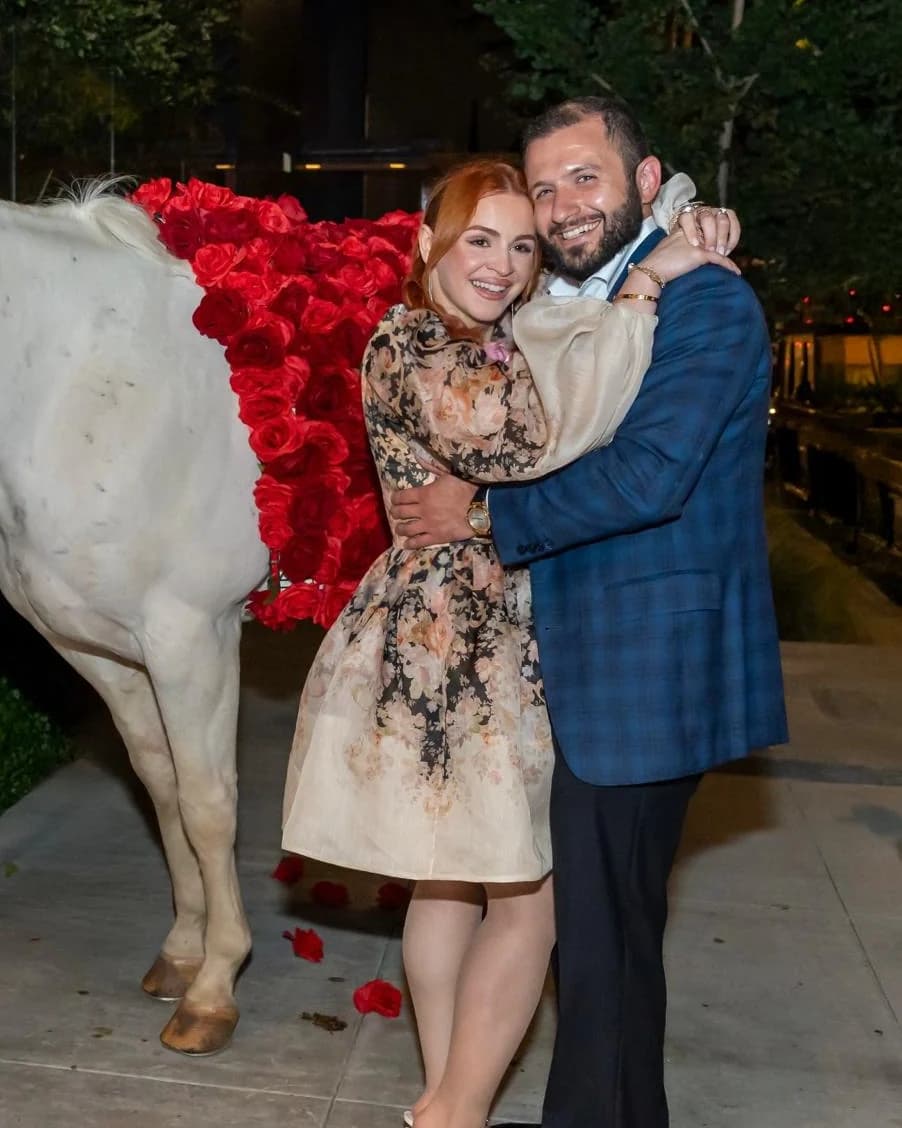 Gevork and Lusine smiling together beside a white horse and a bed of red roses